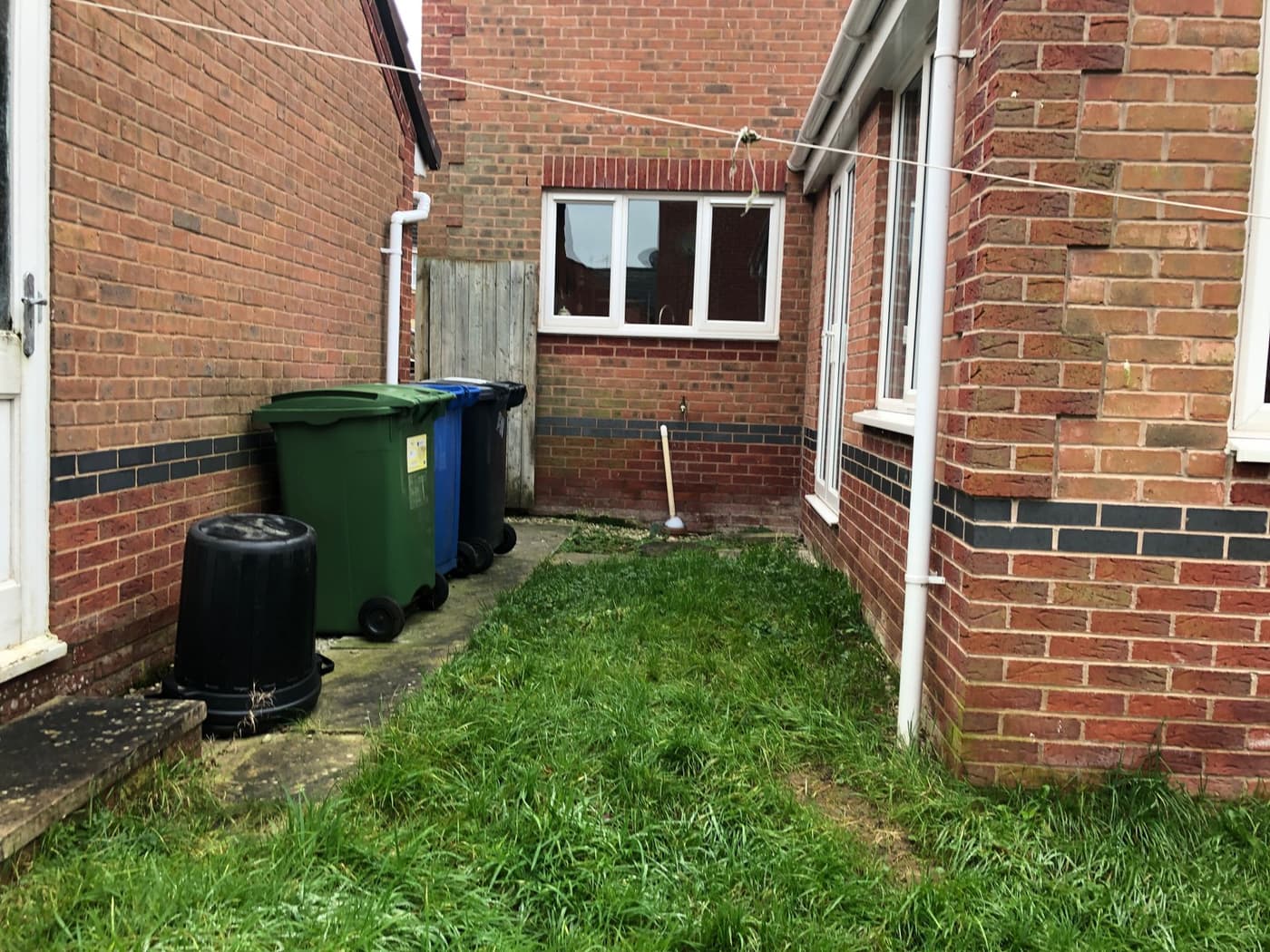 Overgrown side garden in Grappenhall before landscaping, with wheelie bins on cracked paving and long grass