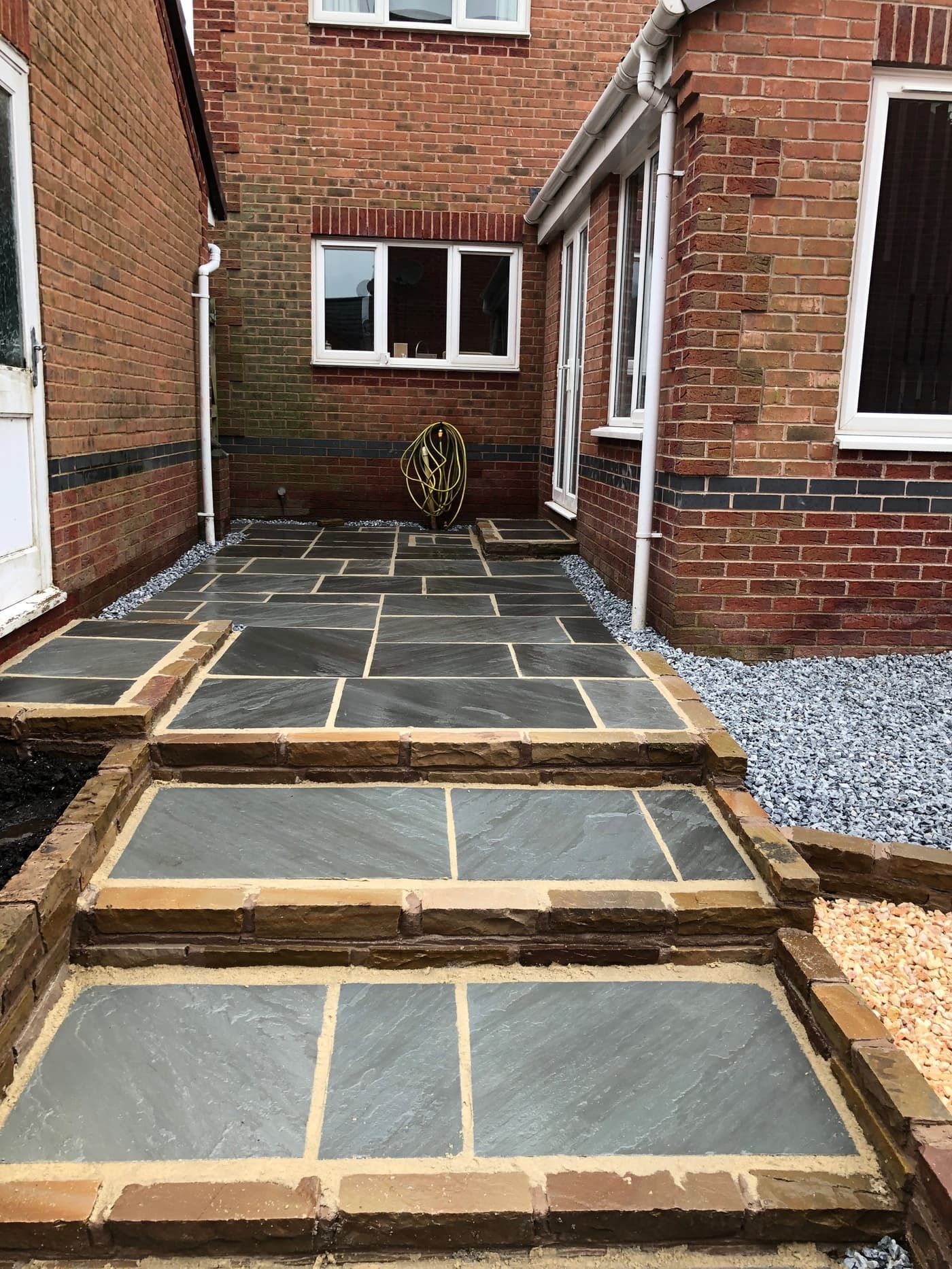 Slate-effect Indian sandstone steps and patio leading up to a red-brick Grappenhall home after landscaping