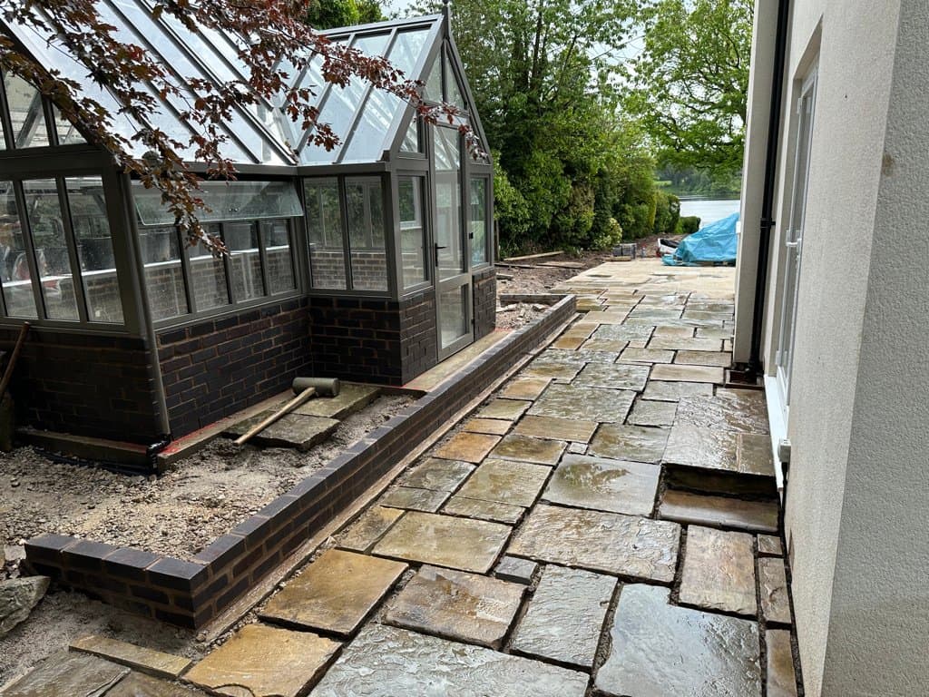 New sandstone patio being laid beside a period conservatory during a luxury garden transformation