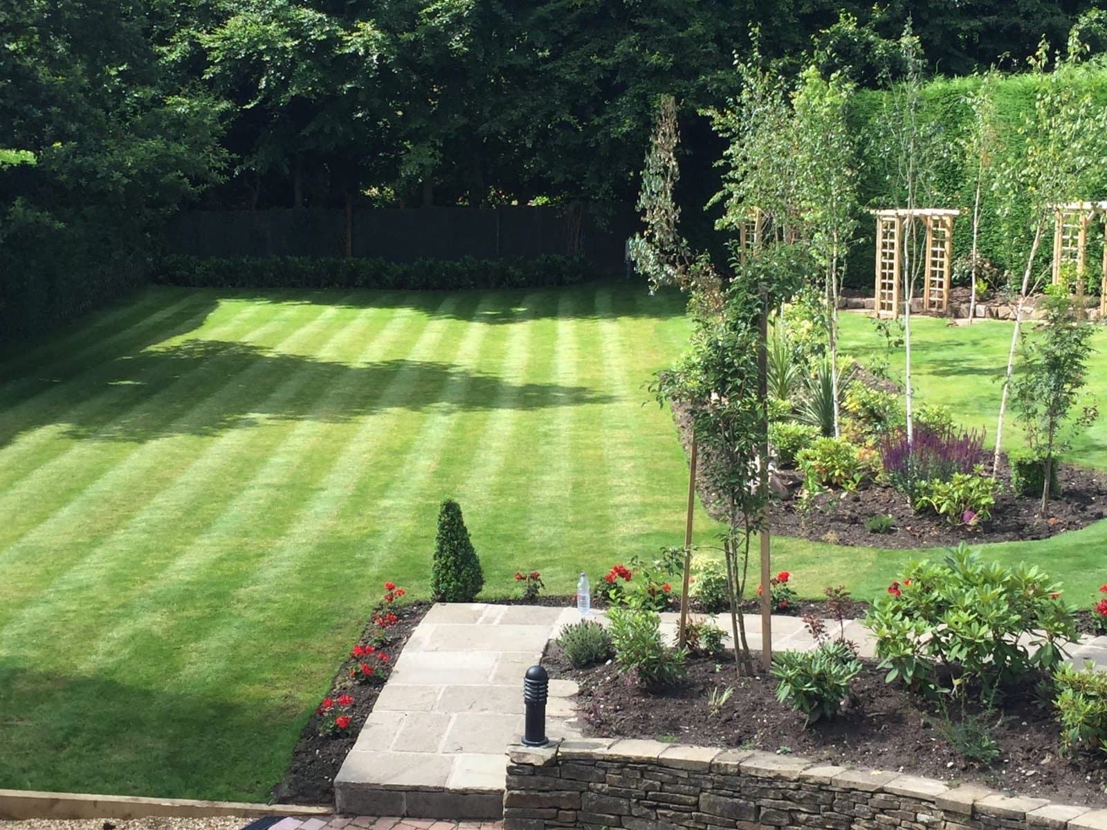 Manicured striped lawn with island beds and trellis arches in a Cheshire garden
